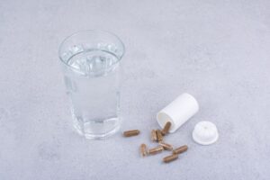 compléments alimentaires posés à côté d’un verre d’eau