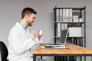 Un médecin souriant en blouse blanche est assis à son bureau et présente des flacons de médicaments devant l'écran de son ordinateur portable lors d'une téléconsultation.